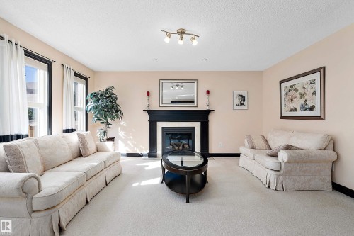 Carpeted living area featuring a fireplace with a black wood-finish mantel, track lighting, and multiple windows - 11515 16 Avenue Sw, Edmonton, AB 