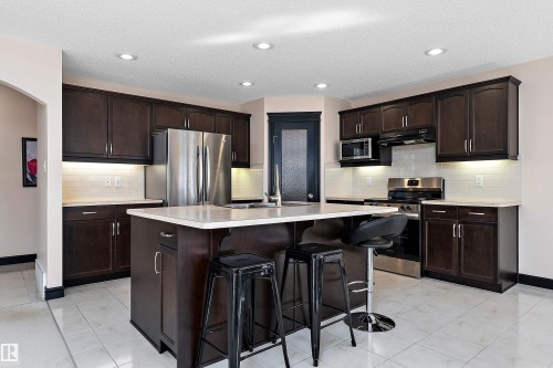 Kitchen featuring dark wood-finish cabinetry, stainless steel appliances, a central island with countertop, tiled flooring, and recessed lighting - 11515 16 Avenue Sw, Edmonton, AB 