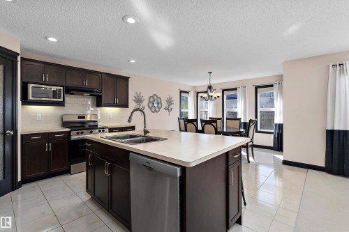 Kitchen featuring dark wood-finish cabinetry, stainless steel appliances, a center island with sink, and tile flooring - 11515 16 Avenue Sw, Edmonton, AB 
