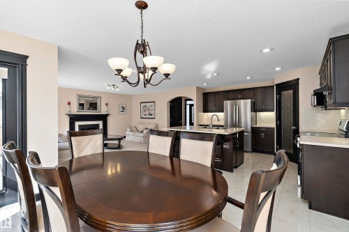 Spacious open-concept layout featuring a decorative fireplace, dark wood cabinetry, white subway tile backsplash, stainless steel appliances, and recessed lighting - 11515 16 Avenue Sw, Edmonton, AB 