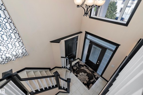 Two-story entry with a dark-framed glass panel door, tile flooring, and a chandelier - 11515 16 Avenue Sw, Edmonton, AB 