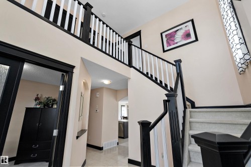 Two-story foyer featuring a carpeted staircase with dark wood-finish newel posts and railings, white balusters, and a recessed archway - 11515 16 Avenue Sw, Edmonton, AB 