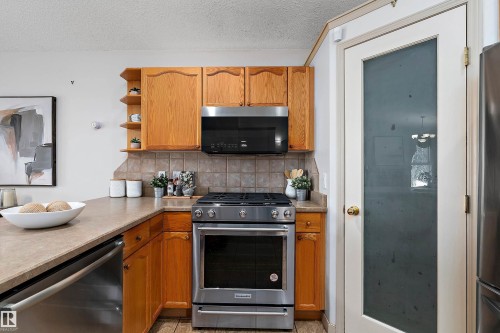 Kitchen featuring wood cabinetry, stainless steel range, built-in microwave, durable countertops, and a full-light door with frosted glass - 1046 Blackburn Close Sw, Edmonton, AB 
