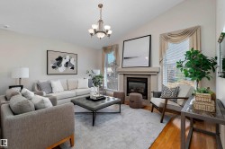 Vaulted ceiling, gas fireplace with tile surround, hardwood flooring, large windows, and a chandelier - 