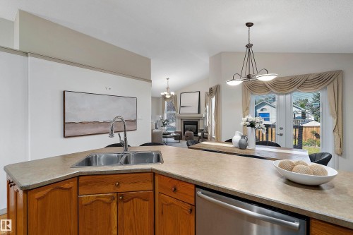 Kitchen island with integrated stainless steel sink, wood cabinetry, and stainless steel dishwasher - 1046 Blackburn Close Sw, Edmonton, AB 