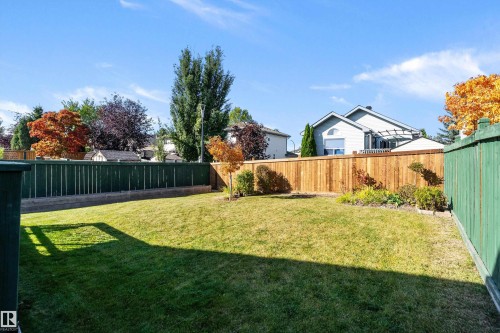 Expansive backyard featuring a manicured lawn, a blend of green and natural wood fencing, and established perimeter landscaping - 1046 Blackburn Close Sw, Edmonton, AB 
