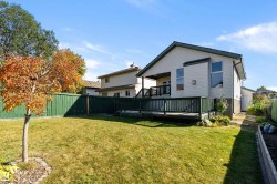 Expansive backyard featuring a green privacy fence, a wood deck with dark railings, a manicured lawn, and mature trees - 