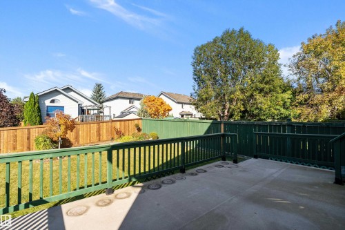 Expansive patio with a green wooden railing, overlooking a fenced backyard with a manicured lawn and mature trees - 1046 Blackburn Close Sw, Edmonton, AB 