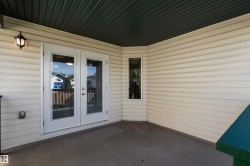 Covered outdoor patio with concrete flooring, accented by a single light fixture, a narrow vertical window, and a pair of white French doors - 