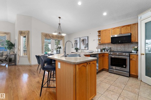 Kitchen featuring wood cabinetry, stainless steel appliances, a center island with bar seating, and tile flooring - 1046 Blackburn Close Sw, Edmonton, AB 