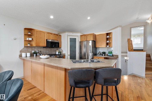 Kitchen featuring light wood cabinetry, stainless steel appliances, a tile backsplash, a kitchen island with seating, and wood-finish flooring - 1046 Blackburn Close Sw, Edmonton, AB 