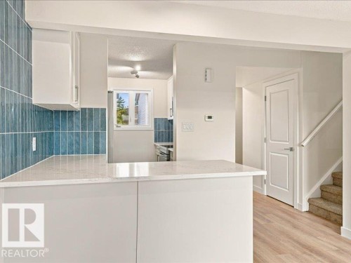 Quartz countertop, white cabinetry, blue vertical tile backsplash, wood-finish flooring, and white interior doors - 18325 66 Avenue Nw, Edmonton, AB 