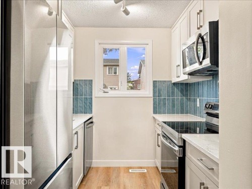 White cabinetry with brushed nickel hardware, stainless steel appliances, blue subway tile backsplash, white countertops, and wood-finish flooring - 18325 66 Avenue Nw, Edmonton, AB 