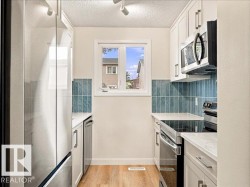 White cabinetry with brushed nickel hardware, stainless steel appliances, blue subway tile backsplash, white countertops, and wood-finish flooring - 
