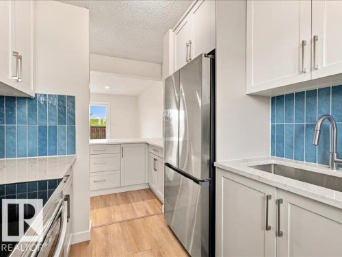 White shaker cabinetry, light wood-finish flooring, stainless steel appliances, a blue tile backsplash, and light-toned countertops - 18325 66 Avenue Nw, Edmonton, AB 