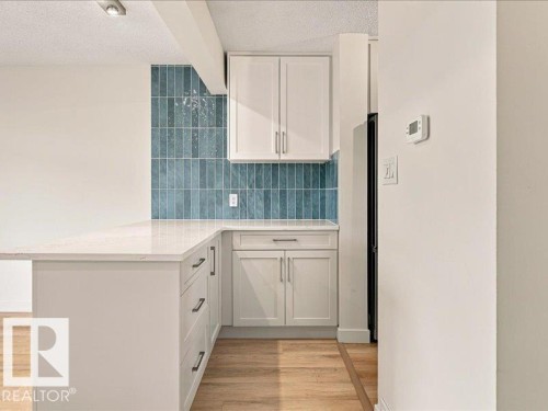 White cabinetry with chrome hardware, full-height blue subway tile backsplash, light-toned countertops, and wood-finish flooring - 18325 66 Avenue Nw, Edmonton, AB 