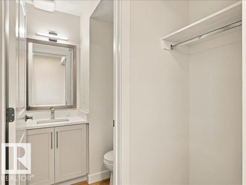 White vanity with brushed nickel hardware, quartz countertop, undermount sink, wall-mounted light fixture, and framed mirror - 18325 66 Avenue Nw, Edmonton, AB 
