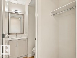 White vanity with brushed nickel hardware, quartz countertop, undermount sink, wall-mounted light fixture, and framed mirror - 