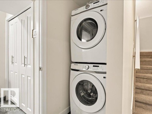 Stacked laundry appliances with white finishes, bi-fold closet doors, and carpeted stairs - 18325 66 Avenue Nw, Edmonton, AB 