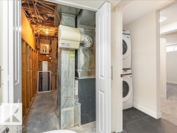Utility area featuring a stacked washer and dryer, exposed ductwork, and an electrical panel - 