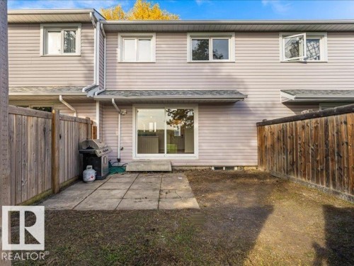 Fenced backyard with a concrete patio, sliding glass door, and upper-level windows - 18325 66 Avenue Nw, Edmonton, AB 