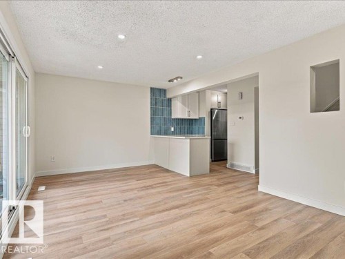 Wood-finish flooring, recessed lighting, sliding glass door, kitchen with light cabinetry, and blue tiled backsplash - 18325 66 Avenue Nw, Edmonton, AB 