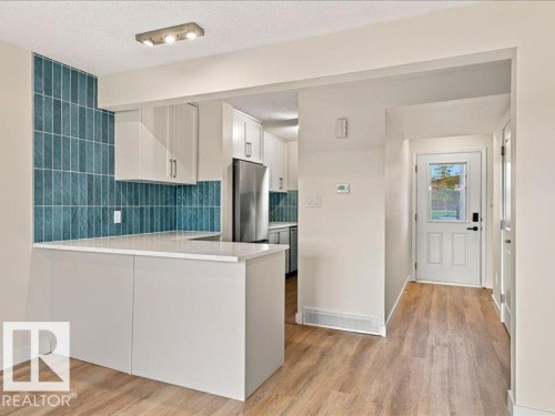 Breakfast bar with white countertop, subway tile backsplash, wood-finish flooring, white cabinetry, and stainless steel refrigerator - 18325 66 Avenue Nw, Edmonton, AB 