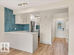 Breakfast bar with white countertop, subway tile backsplash, wood-finish flooring, white cabinetry, and stainless steel refrigerator - 