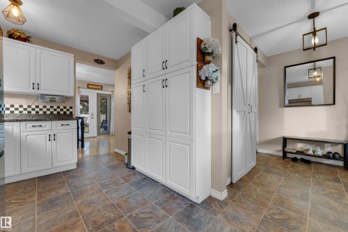 White cabinetry with black hardware, checkered backsplash, dark stone-finish countertops, and barn door entry - 1920 145 Avenue Nw, Edmonton, AB 