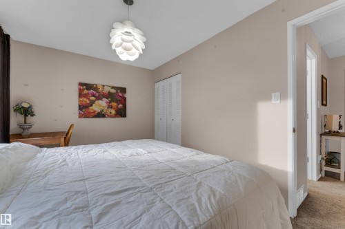 White bi-fold closet doors, contemporary ceiling fixture, carpet flooring, light neutral wall color, and a wood-finish desk - 1920 145 Avenue Nw, Edmonton, AB 