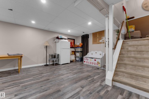 Recessed lighting illuminates the wood-finish flooring in this versatile space, featuring a staircase with a wood handrail - 1920 145 Avenue Nw, Edmonton, AB 