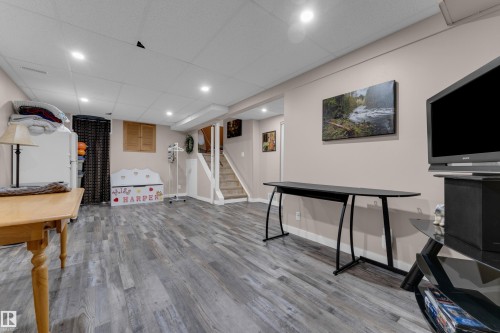 Spacious room featuring wood-finish flooring, recessed lighting, neutral wall tones, and a staircase with white risers and handrails - 1920 145 Avenue Nw, Edmonton, AB 