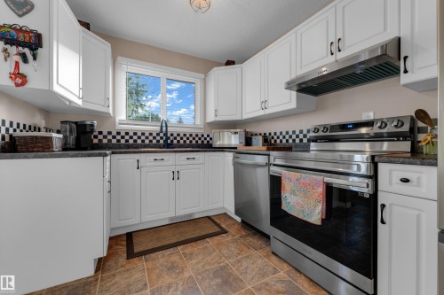 Kitchen featuring white cabinetry, stone-finish countertops, stainless steel appliances, a checkered tile backsplash, and tile flooring - 1920 145 Avenue Nw, Edmonton, AB 