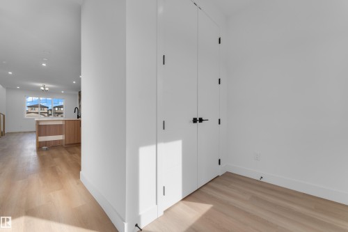Light wood-finish flooring, white walls, recessed lighting, and a kitchen island with a black faucet - 512 Robinson Boulevard, Leduc, AB 