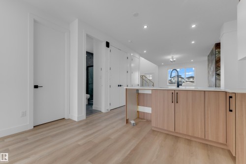 Wood-finish flooring throughout, kitchen island with light wood cabinetry and black hardware, white countertop, recessed lighting, and a modern black faucet - 512 Robinson Boulevard, Leduc, AB 