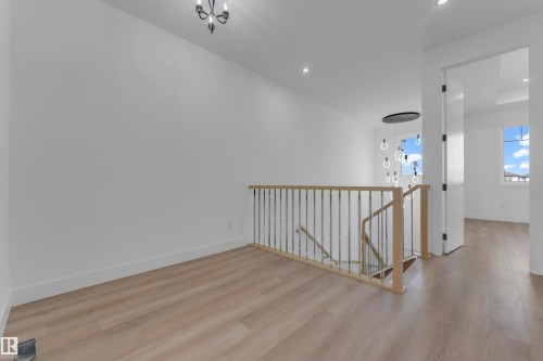 Wood-finish flooring throughout, modern light fixture, recessed lighting, white trim, and a contemporary stair railing with metal spindles - 512 Robinson Boulevard, Leduc, AB 