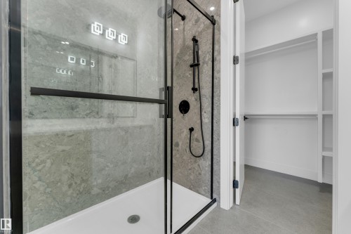 Glass-enclosed shower with matte black fixtures, stone-finish tile surround, and white shower pan - 512 Robinson Boulevard, Leduc, AB 
