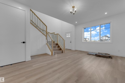 High ceilings with recessed lighting, wood-finish flooring, a contemporary staircase with wood and metal railing, and a large multi-pane window - 512 Robinson Boulevard, Leduc, AB 