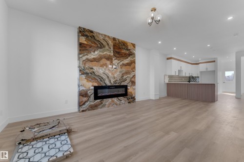 Hardwood-finish flooring, recessed lighting, and a modern linear electric fireplace with a floor-to-ceiling stone surround - 512 Robinson Boulevard, Leduc, AB 