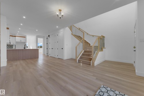 High ceilings, wood-finish flooring, two-tone kitchen cabinetry, built-in kitchen island, and a staircase with metal railings - 512 Robinson Boulevard, Leduc, AB 