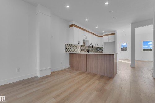 Kitchen featuring light wood-finish flooring, white cabinetry, a patterned tile backsplash, and an island with a matte black faucet - 512 Robinson Boulevard, Leduc, AB 