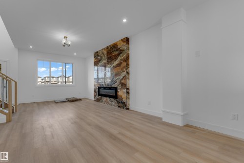 Wood-finish flooring, accent wall with a built-in fireplace, staircase with wood handrails, large window, and recessed lighting - 512 Robinson Boulevard, Leduc, AB 