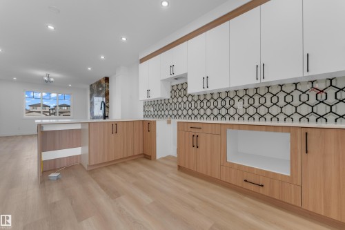 Kitchen featuring wood-finish lower cabinetry, white upper cabinetry, and a geometric pattern tile backsplash - 512 Robinson Boulevard, Leduc, AB 
