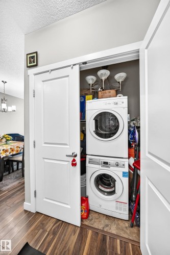 Laundry closet featuring a stackable washer and dryer, wood-finish flooring, white doors, and brushed nickel hardware - #404 12804 140 Av Nw, Edmonton, AB 