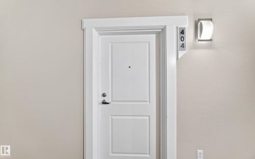 White interior door with paneling, contrasting door trim, and a wall-mounted light fixture - #404 12804 140 Av Nw, Edmonton, AB 