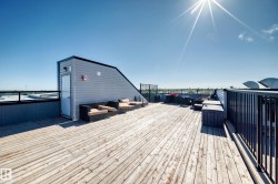 Expansive rooftop deck featuring wood-finish flooring, a contemporary black railing, and a sloped structure with light gray siding - 