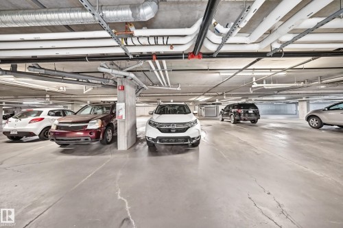 Underground parking facility with concrete flooring, exposed ceiling utilities, and fluorescent lighting - #404 12804 140 Av Nw, Edmonton, AB 