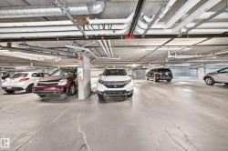 Underground parking facility with concrete flooring, exposed ceiling utilities, and fluorescent lighting - 
