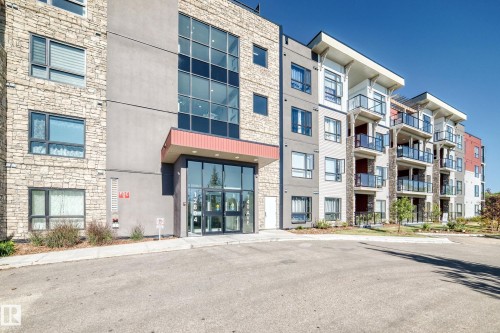 Modern multi-story building featuring a stone and stucco facade, large windows, glass-paneled balconies, and a prominent glass entrance with an overhang - #404 12804 140 Av Nw, Edmonton, AB 
