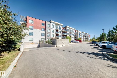Multi-story building featuring balconies, a covered parking entrance, and an expansive exterior parking area - #404 12804 140 Av Nw, Edmonton, AB 